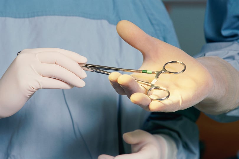 Nurse handing surgeon pair of clamps during surgery